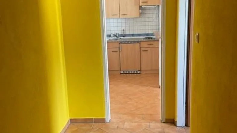 Heller Flur mit gelben Wänden und Fliesenboden, der zu einer Küche führt.