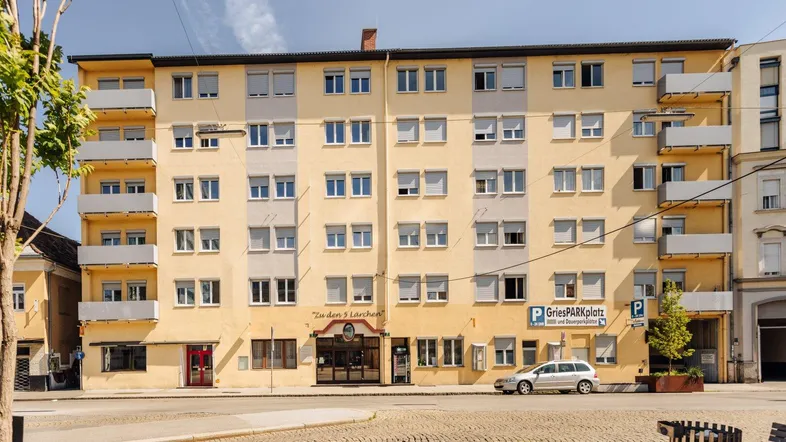 Gelbes Mehrfamilienhaus mit vielen Fenstern und Balkonen an einer städtischen Straße.