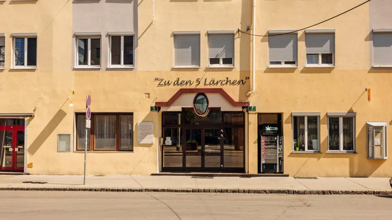 Gelbe Fassade eines Mehrfamilienhauses mit vielen Fenstern und einem Eingangsbereich an der Straße.