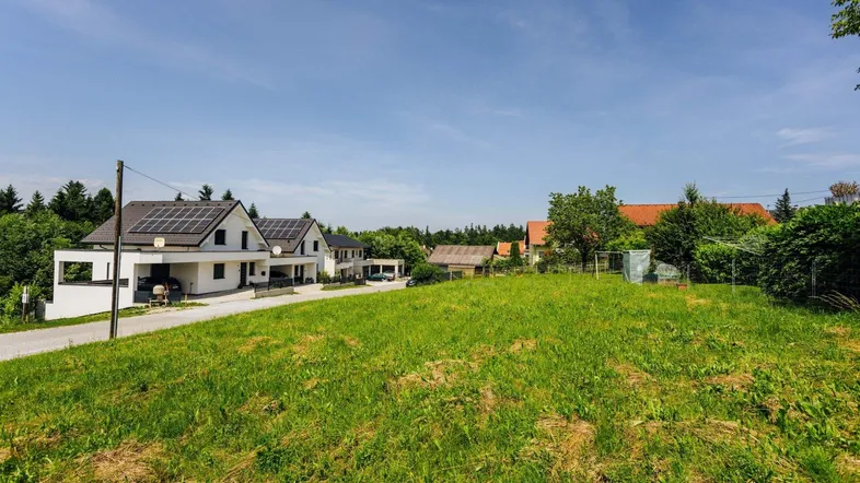 Grünes Grundstück mit Blick auf moderne Häuser und ländliche Umgebung unter blauem Himmel.