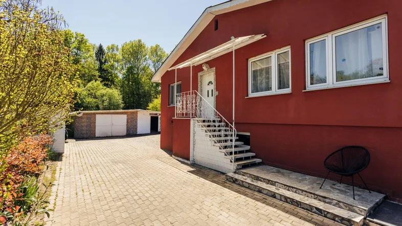 Rotes Einfamilienhaus mit weißer Eingangstür, Außentreppe und gepflasterter Auffahrt.