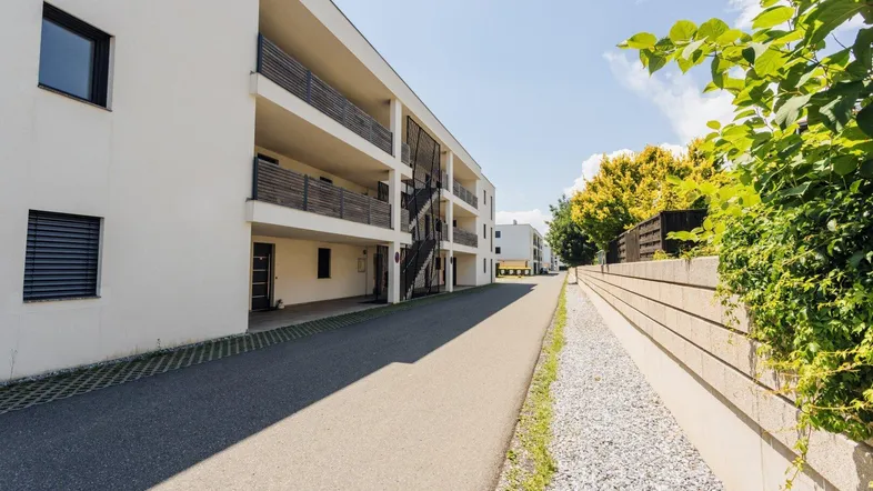 Modernes Mehrfamilienhaus mit weißer Fassade, Balkonen und gepflegter Außenanlage unter blauem Himmel.