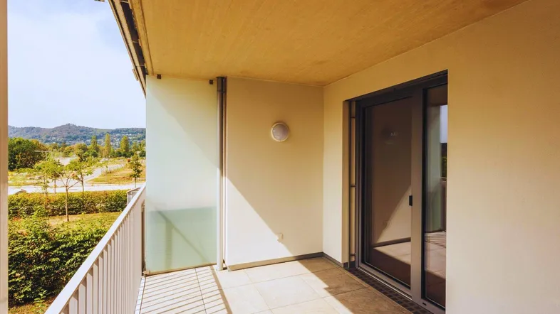 Heller Balkon mit Fliesenboden und Glasbrüstung, bietet einen weiten Blick ins Grüne und auf Hügel.
