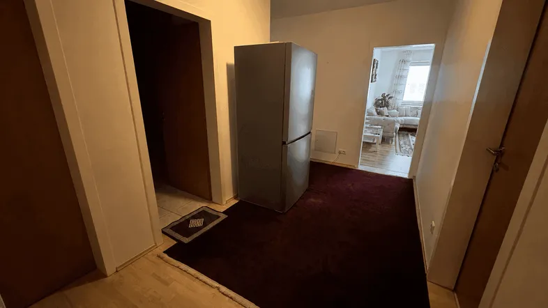 Geräumiger Flur mit Teppichboden und einem großen Kühlschrank, der zu den Wohnbereichen führt.
