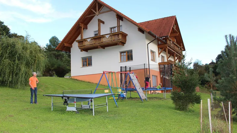 Großes Einfamilienhaus mit Holzfassade und rotem Dach, umgeben von einem weitläufigen Garten mit Spielgeräten.