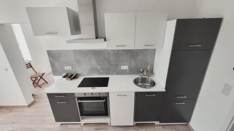 Moderne Einbauküche mit grauen und weißen Schränken, Induktionskochfeld und Backofen in einem hellen Raum.