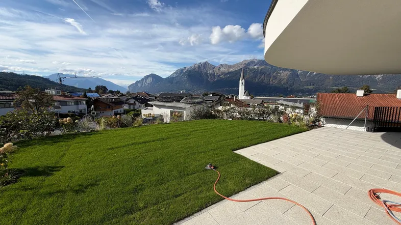Großer gepflegter Rasenbereich mit weitläufiger Terrasse und beeindruckendem Bergblick über die Stadt.