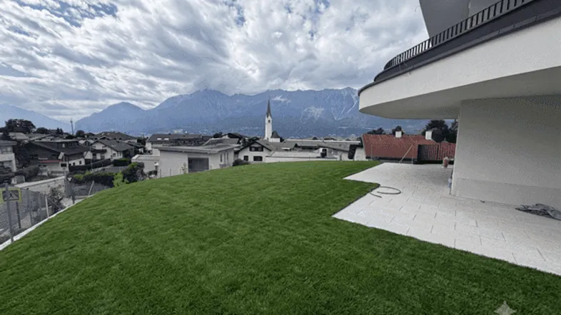 Frisch angelegter Rasenbereich mit moderner Architektur und beeindruckendem Bergblick im Hintergrund.