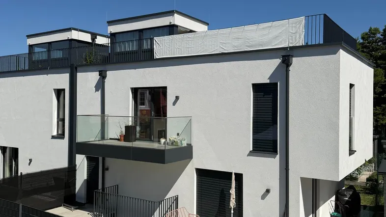 Moderne Wohnanlage mit weißer Fassade, Balkonen und Terrassen unter blauem Himmel.
