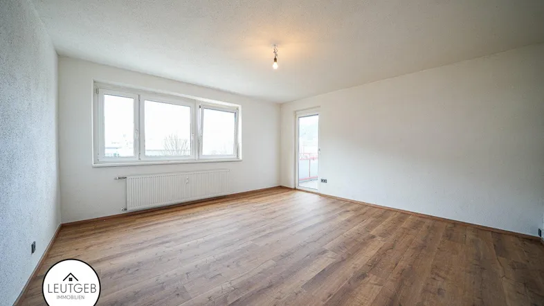 Helles, leeres Zimmer mit Laminatboden und Zugang zum Balkon.