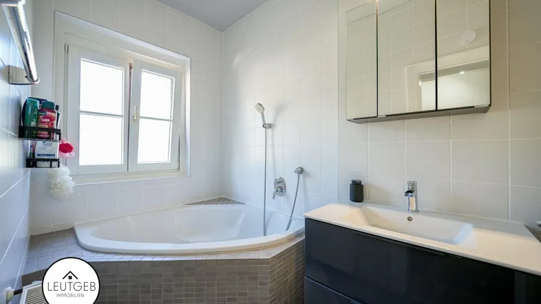 Helles Badezimmer mit Eckbadewanne, modernem Waschtisch und Spiegelschrank, sowie einem Fenster für Tageslicht.