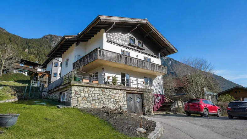 Alpines Haus mit Steinsockel, Holzbalkonen und Bergblick in sonniger Lage.