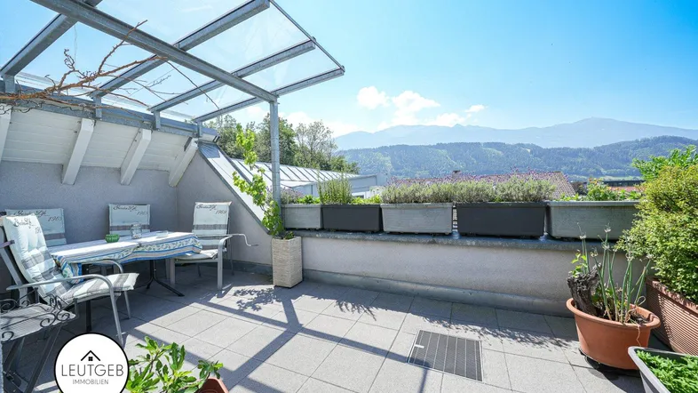 Geräumige Dachterrasse mit Sitzgelegenheiten, Pflanzen und einem beeindruckenden Bergblick unter einem Glasdach.