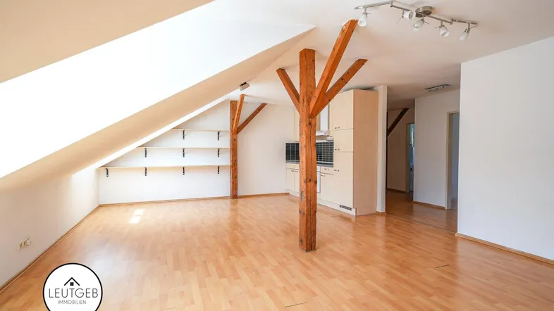 Heller Dachgeschossraum mit sichtbaren Holzbalken, Laminatboden und integrierter Küchenzeile.