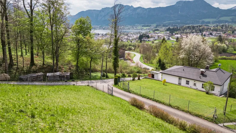 Haus mit großem Garten, Zufahrt und weitem Blick auf See und Berge in ländlicher Umgebung.