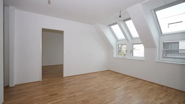Helles Zimmer mit Dachschrägen, Parkettboden und mehreren Dachfenstern, ideal als Wohn- oder Schlafbereich.