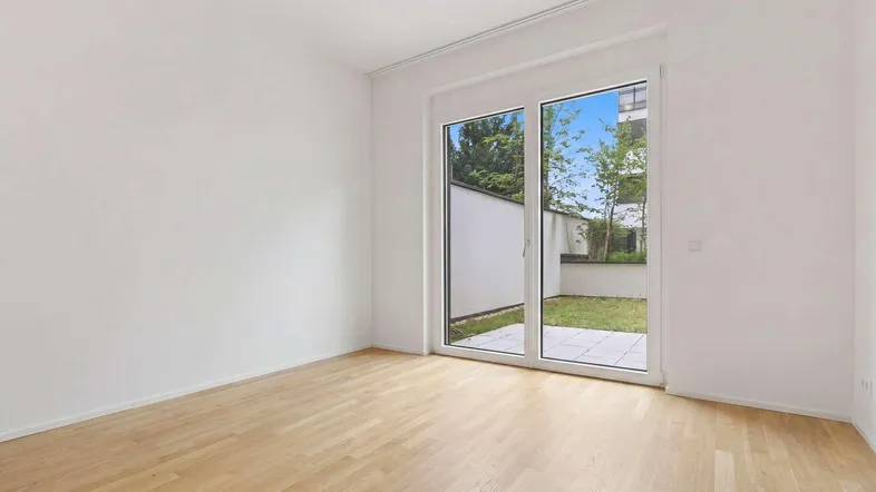 Heller Raum mit Parkettboden und Zugang zu einer kleinen Terrasse und Garten.