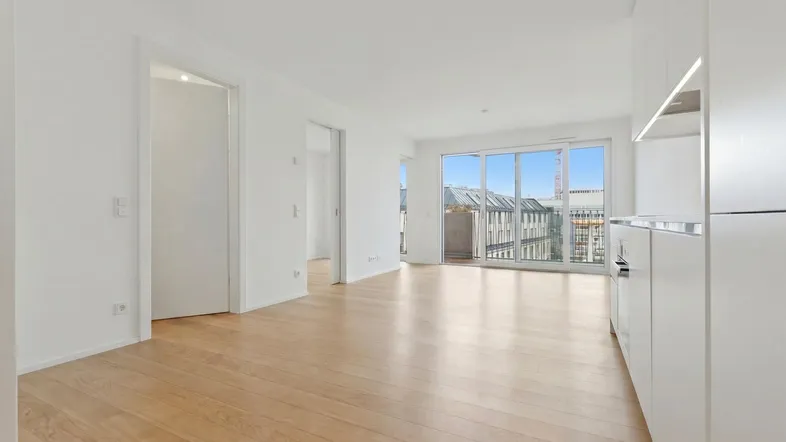Helles Wohnzimmer mit Parkettboden, weißen Wänden und Zugang zu einem Balkon.