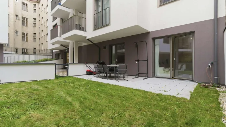 Gepflasterte Terrasse mit Gartenmöbeln und Rasenfläche im Außenbereich eines modernen Gebäudes.