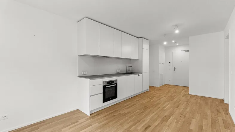 Moderne weiße Einbauküche mit Backofen und Holzboden in einem offenen Wohnbereich.