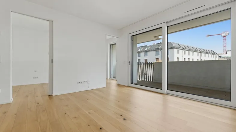 Helles Zimmer mit Holzboden und Zugang zu einem Balkon, bietet einen Blick auf die Stadt.