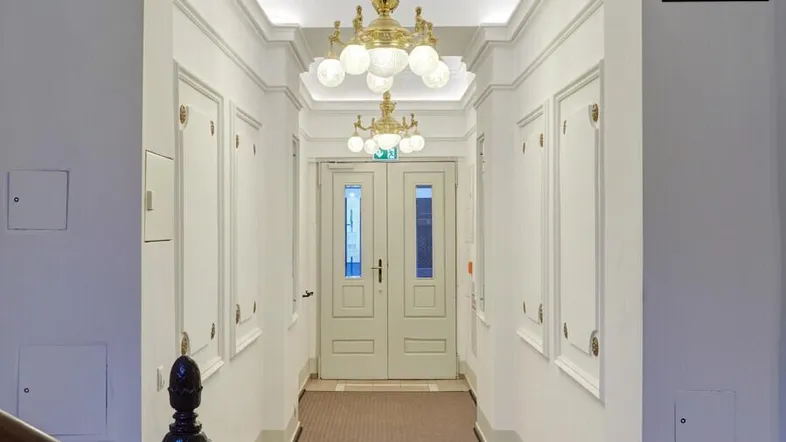 Heller Flur im Erdgeschoss mit eleganten Kronleuchtern und Teppichboden, der zu einer Doppeltür führt.