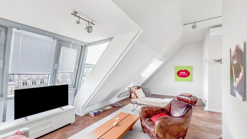 Helles Wohnzimmer im Dachgeschoss mit schrägen Wänden, Parkettboden und Blick auf die Stadt.