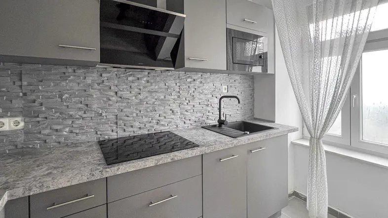 Moderne Küche in Grau mit Steinoptik-Arbeitsplatte, Induktionskochfeld und integrierter Mikrowelle.