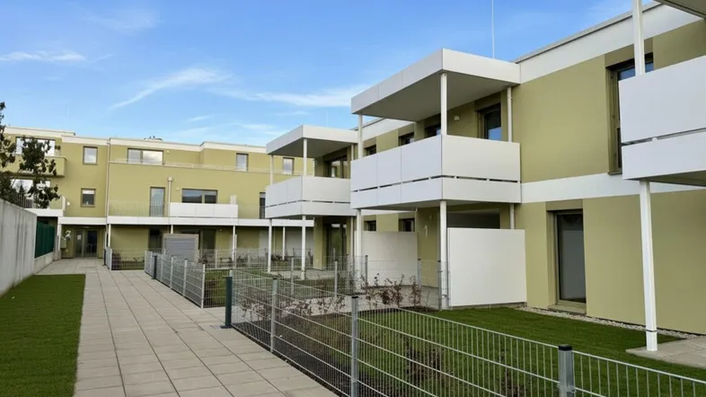 Moderne Wohnanlage mit hellgrüner Fassade, Balkonen und kleinen Rasenflächen unter blauem Himmel.