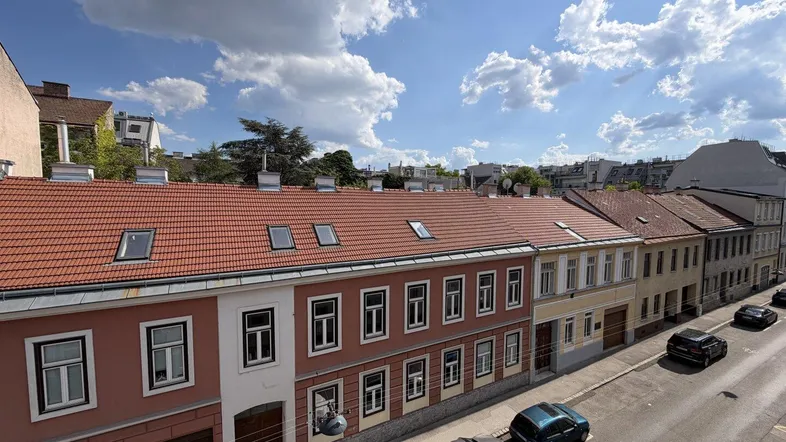 Panoramablick auf eine Wohnstraße mit geparkten Autos und traditionellen Gebäuden unter blauem Himmel.