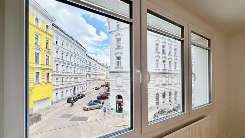 Blick aus einem Fenster auf eine belebte Stadtstraße mit historischen Gebäuden und parkenden Autos.