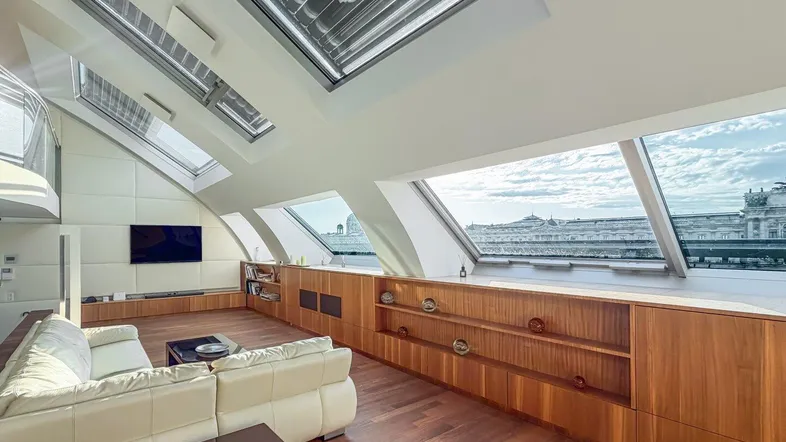 Helles Wohnzimmer im Dachgeschoss mit Holzboden, großen Dachfenstern und weitem Stadtblick.