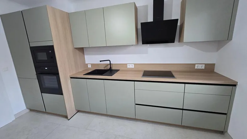 Moderne Einbauküche in Hellgrün mit Holzarbeitsplatte, integrierten Geräten und Dunstabzugshaube.