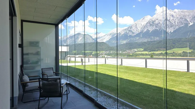 Verglaste Terrasse mit modernen Outdoor-Möbeln und beeindruckendem Bergblick.