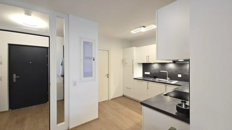 Moderne Küche mit hellen Schränken, dunkler Arbeitsplatte und Holzboden, angrenzend an den Eingangsbereich.