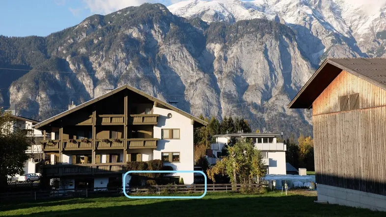 Alpines Gebäude mit traditionellen Holzbalkonen und schneebedeckten Bergen im Hintergrund.