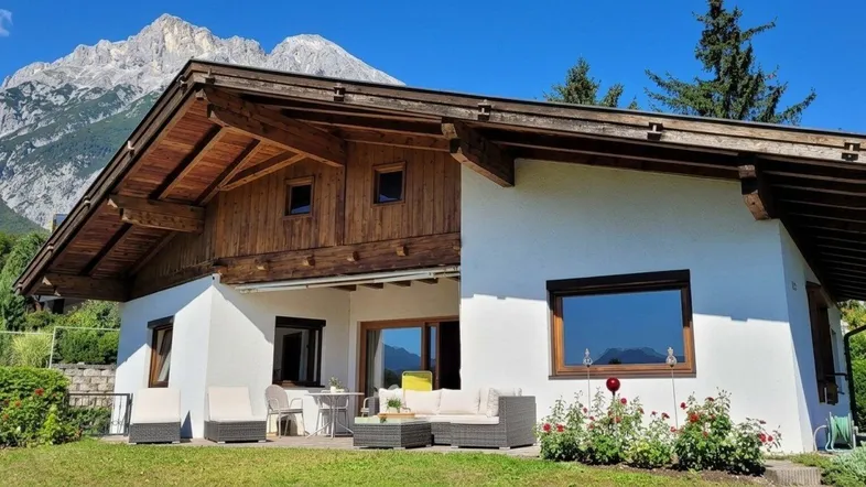 Charmantes Haus im alpinen Stil mit weißer Fassade, Holzverkleidung und einer möblierten Terrasse mit Bergblick.