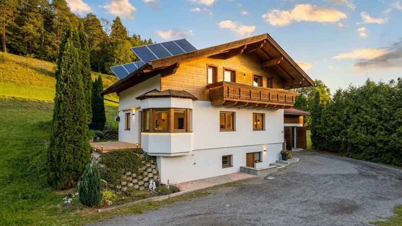 Charmantes Chalet mit traditioneller Holzfassade, Balkon und Photovoltaikanlage vor malerischer Bergkulisse.