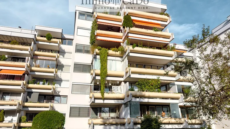Mehrstöckiges Apartmentgebäude mit zahlreichen begrünten Balkonen und einer gepflegten Rasenfläche davor.
