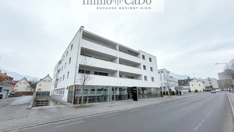 Modernes Mehrfamilienhaus mit weißer Fassade und großen Fenstern an einer Straße gelegen.