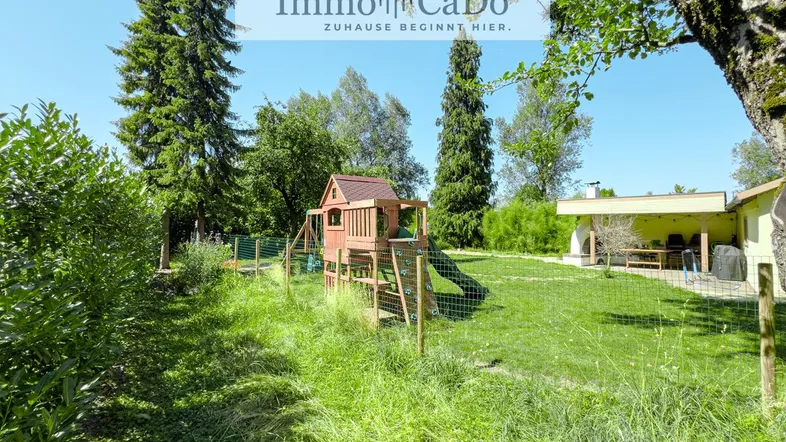 Großer Garten mit Spielplatz, viel Grünfläche und einem überdachten Essbereich im Freien.