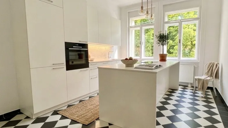 Moderne Küche mit weißen Schränken, Kochinsel und markantem schwarz-weißem Fliesenboden, bietet einen schönen Blick ins Grüne.