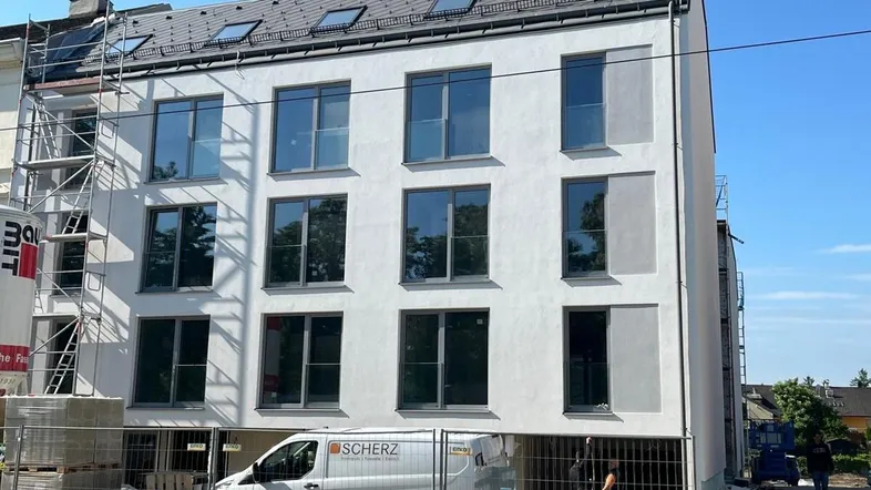 Moderne Neubaufassade mit großen Fenstern und Gerüst im Bauzustand unter blauem Himmel.
