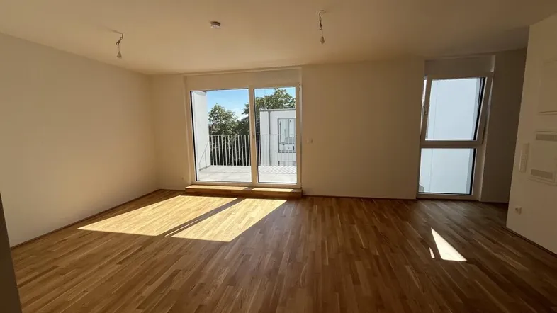 Helles Wohnzimmer mit Parkettboden, großen Fenstern und Zugang zu einem Balkon.