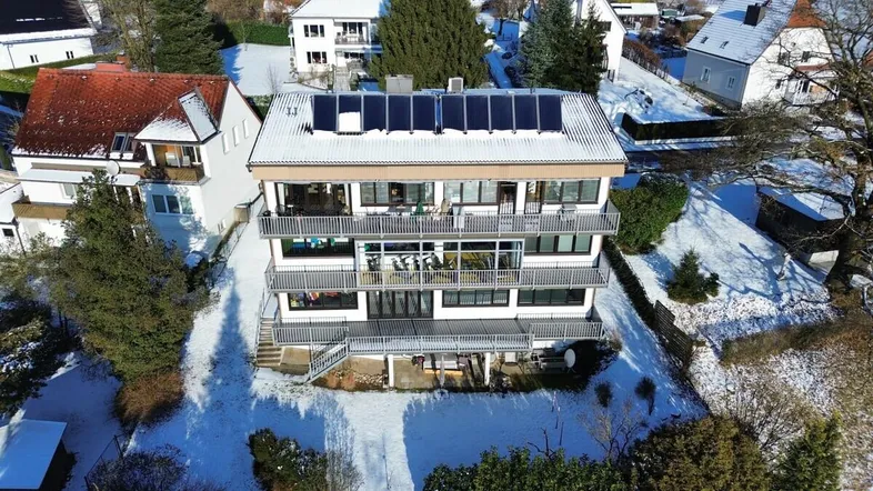 Luftaufnahme eines modernen Mehrfamilienhauses mit Solarpaneelen auf dem Dach und Balkonen im Winter.