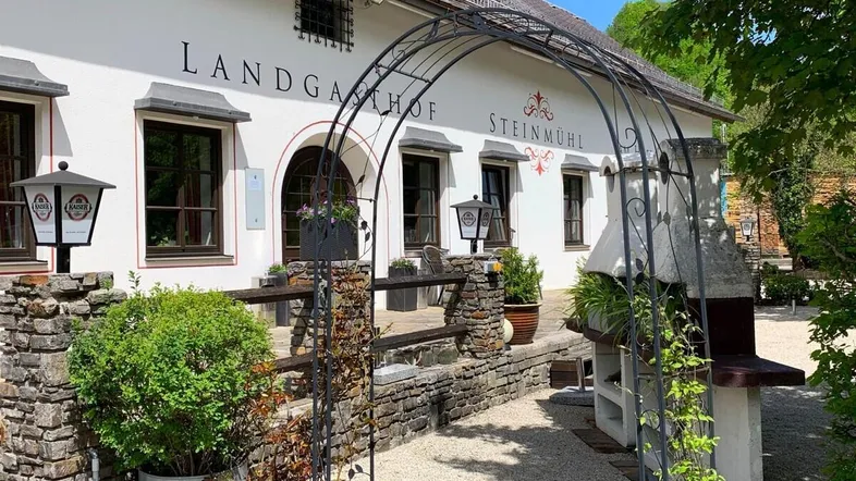 Traditionelles Landgasthofgebäude mit Steinmauern, einem schmiedeeisernen Torbogen und Grillplatz im Freien.