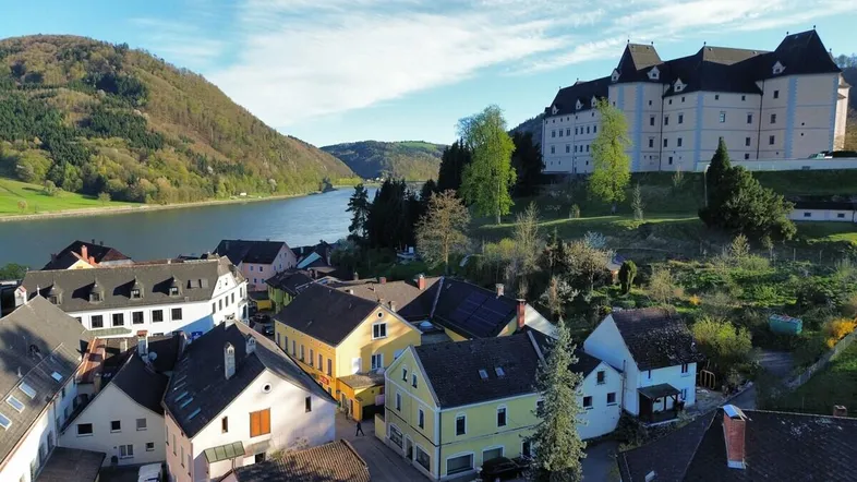 Panoramablick auf eine malerische Stadt am Fluss mit einem historischen Schloss im Hintergrund.