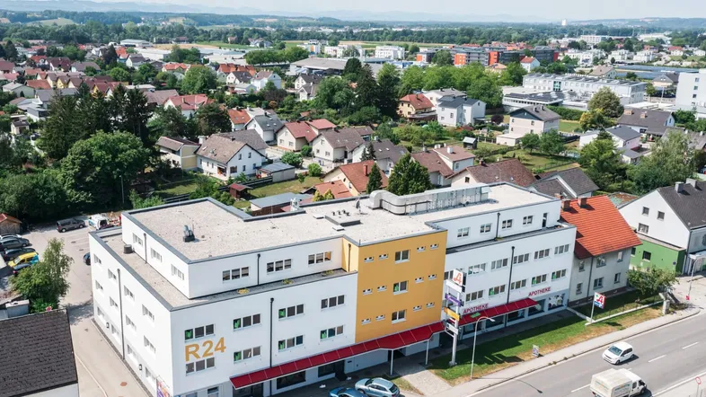 Luftaufnahme eines modernen Geschäftsgebäudes mit gelben Akzenten, umgeben von Wohngebäuden und viel Grün.