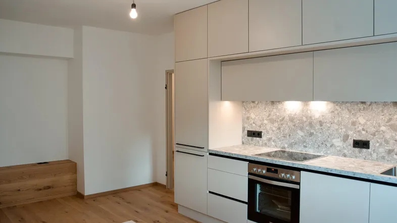 Moderne Einbauküche mit hellen Fronten, integrierten Geräten und Terrazzo-ähnlicher Arbeitsplatte.