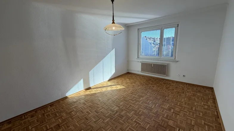 Helles Zimmer mit Parkettboden und großem Fenster, das viel Tageslicht hereinlässt.
